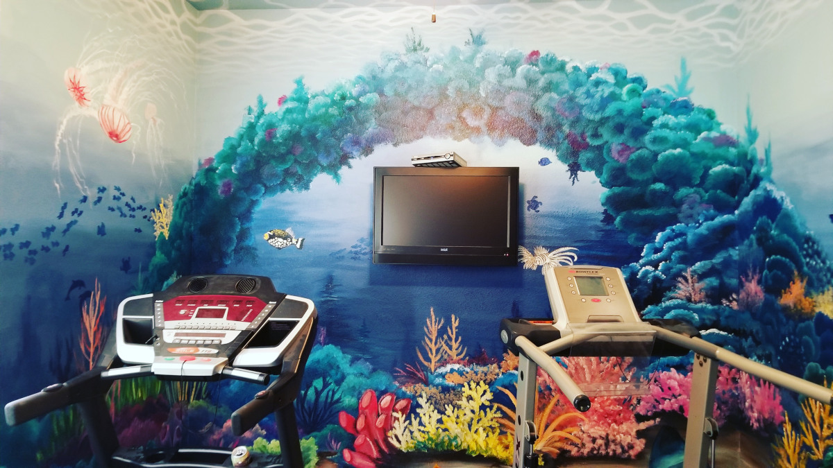 Underwater mural of a coral reef on a home gym wall, with fish, sea turtles, jelly fish, an eel, and an octopus.