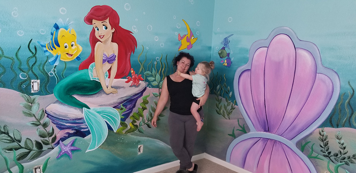 Hayley holding one of the actors in front of a mural from the Disney ad for Little Mermaid’s 30-year anniversary 